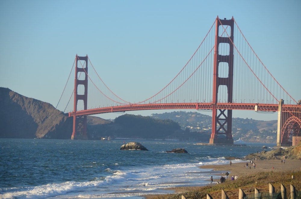 View of Golden Gate Bridge from Baker Beach in San Francisco. View of dogs and people walking on the andy beach in the foreground. 