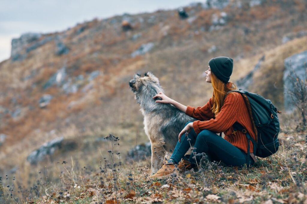 Woman hiking with a wolf dog mix wearing a backpack and looking out over the rocky scenery 