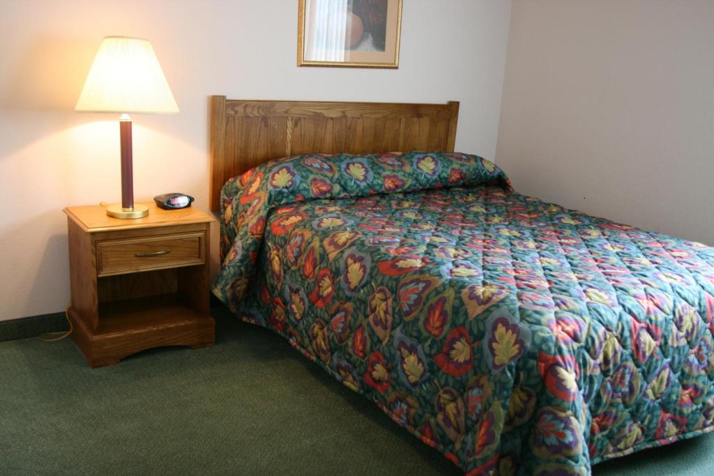 A single bed with a quilted mattress beside a bedside table and a lamp. This is in the Affordable Suites, a pet-friendly hotel in Rocky Mount.