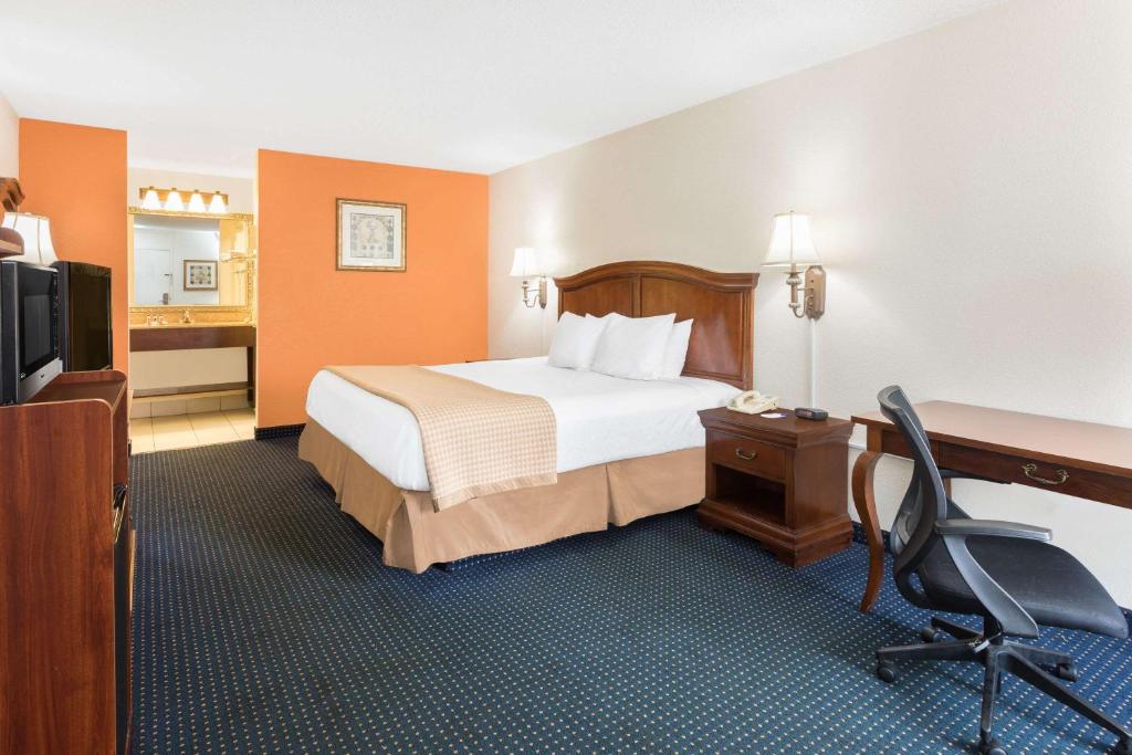 A large bed with white and peach sheets inside a room with white walls and a polka dotted floor. A desk and a swivel chair is placed beside the bed. This is in Baymont by Wyndham in Rocky Mount.