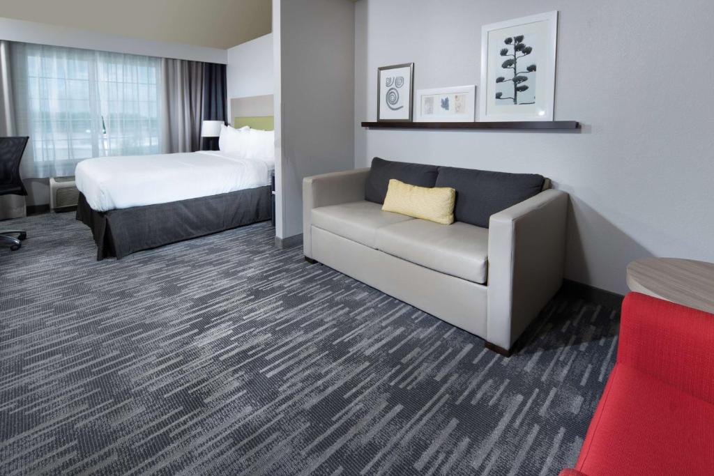 A grey couch beside a bed with white sheets on a room with gray wals and a carpeted floor This is in Country Inn and Suites, a pet friendly hotel in Rocky Mount