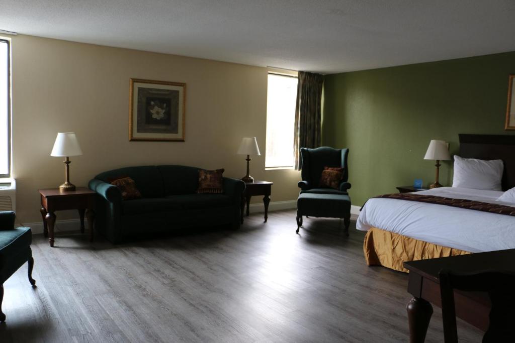 A large bed with white sheets near a couch with tables and lamps on both sides. A single sofa can be seen beside the bed. This is in Days Inn & Suites in Rocky Mount.