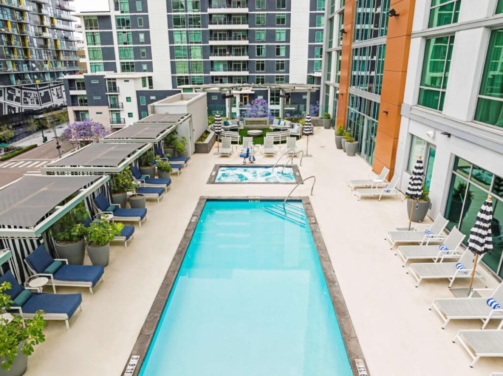 rectangle outdoor pool and jacuzzi on Carte Hotel San Diego Downtown, Curio Collection By Hilton. The pool is surrounded with lounge chairs. it is surrounded with nearby buildings
