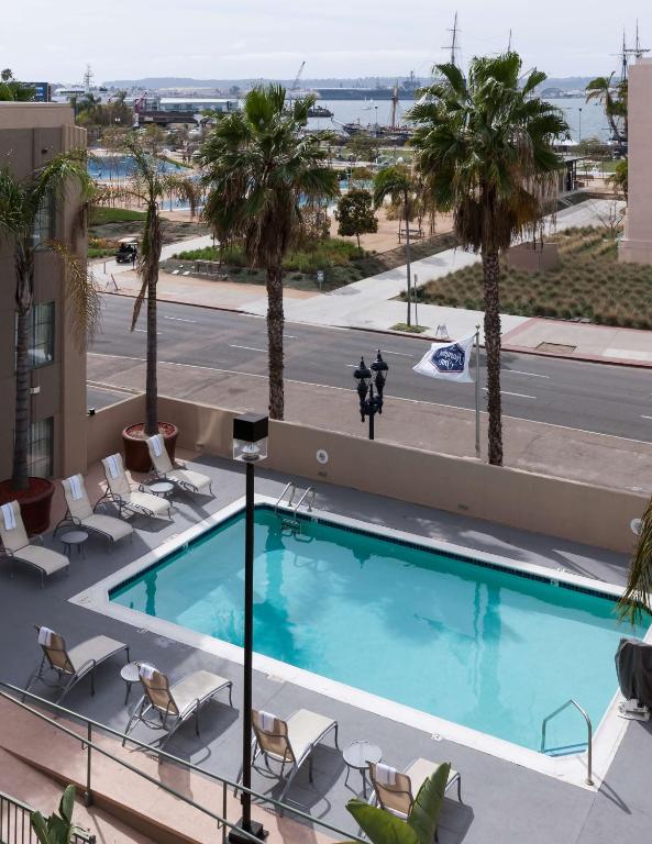 rectangular oudoor pool by the road at Hampton Inn San Diego Downtown. The pool is surrounded with lounge chairs and some palm trees. You can see the harbor from here. 