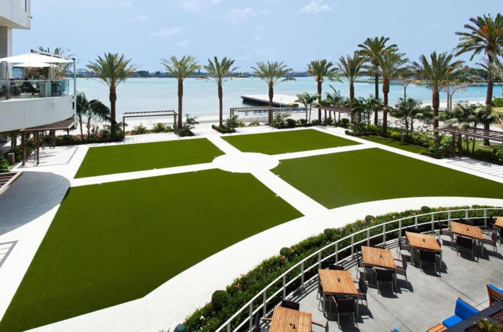 huge outdoor space outside Hilton San Diego Bayfront. There is a dining area overlooking the view of the seafront surrounded by palm tress.
