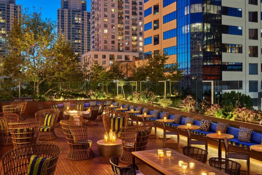 outdoor lounge at Hotel Republic San Diego during night time. Rattan chairs and wooden tables with candles light up the space on a beautiful evening. the area is surrounded with different plants and the view of the nearby buildings.
