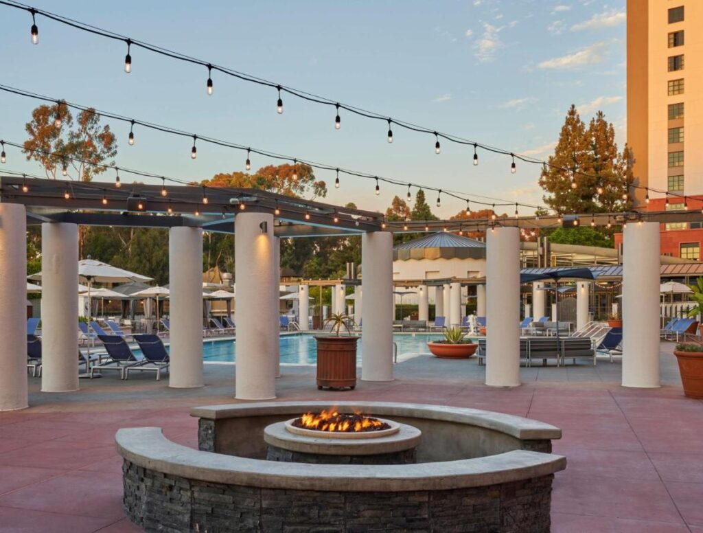 a circular fire pit a few steps from the outdoor pool at Hyatt Regency La Jolla at Aventine. There are 7 big pillars and light bulbs hanging above