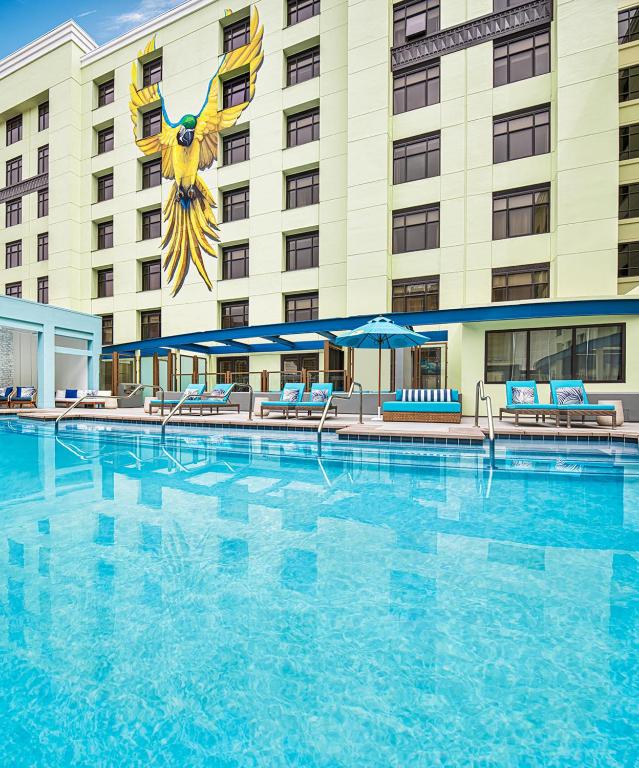 outdoor pool at Margaritaville Hotel San Diego Gaslamp Quarter surroiunded with blue lounge chairs. The hotel building is at the back with a mural of a yellow parrot with its wings open.