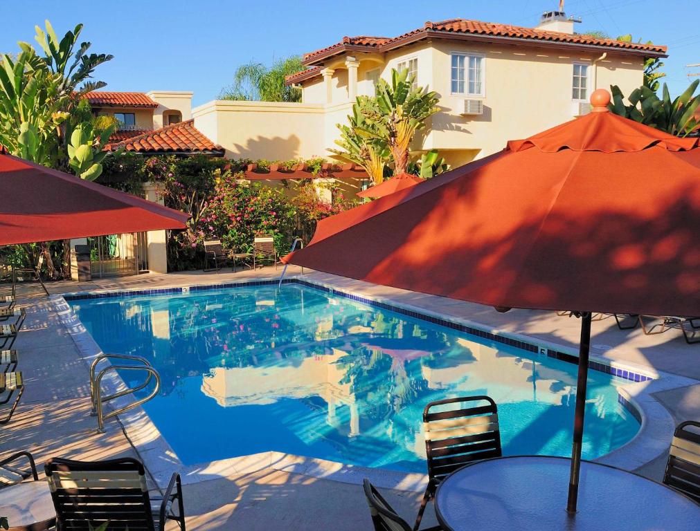 outdoor pool with tables and chairrs on the side with red umbrellas. at the back is the hotel building of Old Town Inn with different plants and trees.