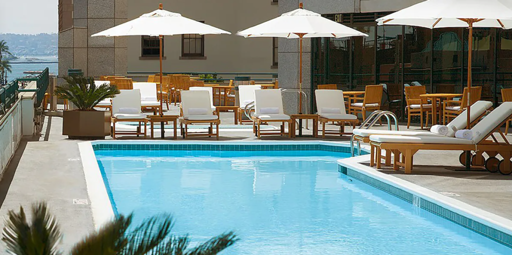 outdoor pool at Westin San Diego Bayview surrouned by white lounge chairs and umbrellas. There are 2 potted plants