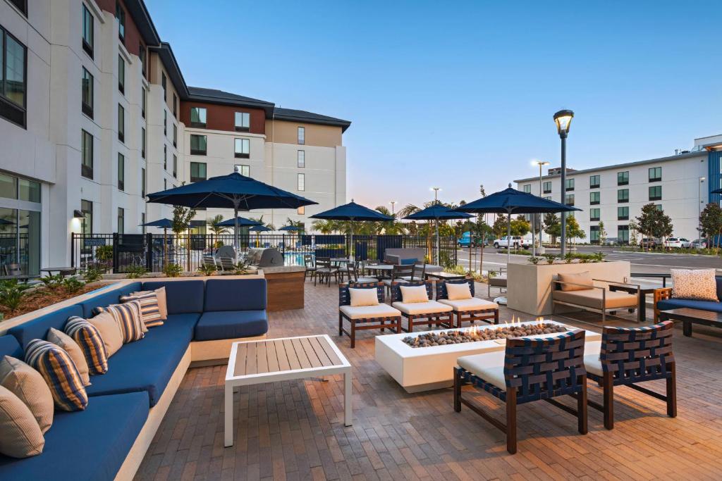 outdoor patio at TownePlace Suites by Marriott San Diego Airport/Liberty Stationwith blue sofas and loung chairs surrouding a fireplace. There are also blue umbrellas to protect from the sun with the hotel building at the back.