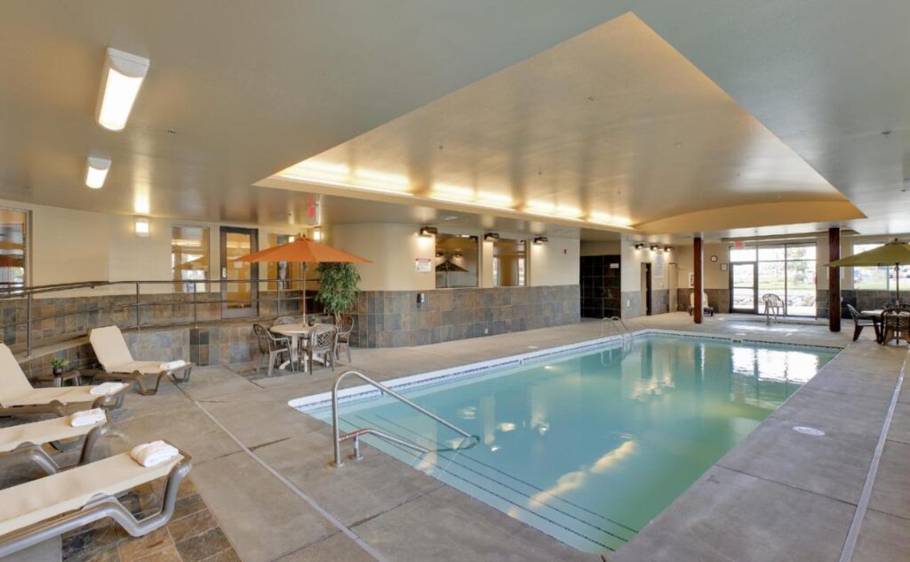 rectangular indoor pool with lounge chairs. there is a table with orange umbrella on the side of the pool at StoneCreek Lodge a pet friendly hotel in missoula